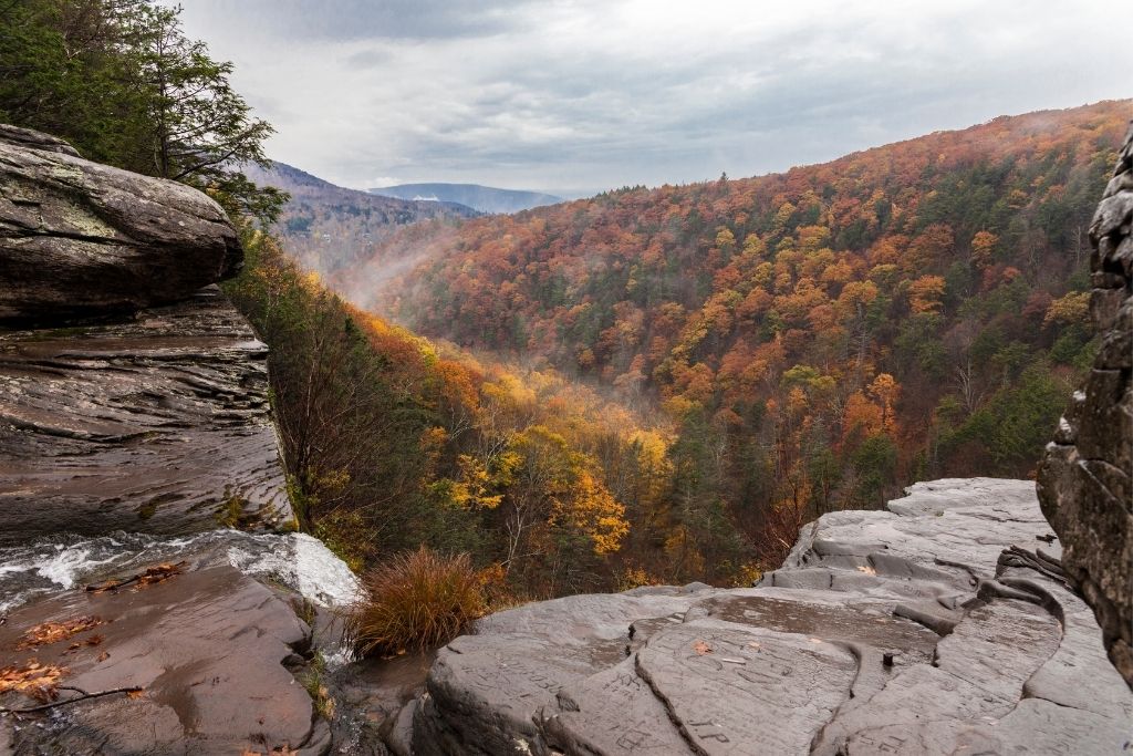 Vibrant fall foliage along a river in the Catskills. A great stop during your New York road trip itinerary.