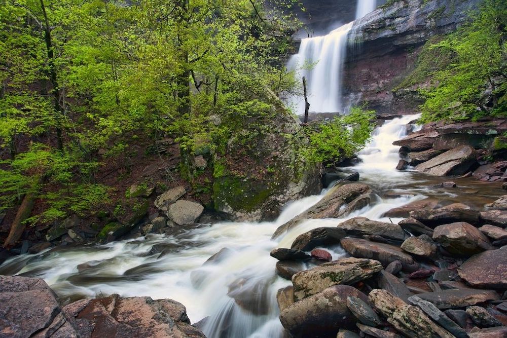 Kaaterskills Waterfall cascading down the rocky slope with green trees surrounding it in Catskills NY has one of the best swimming holes in NY