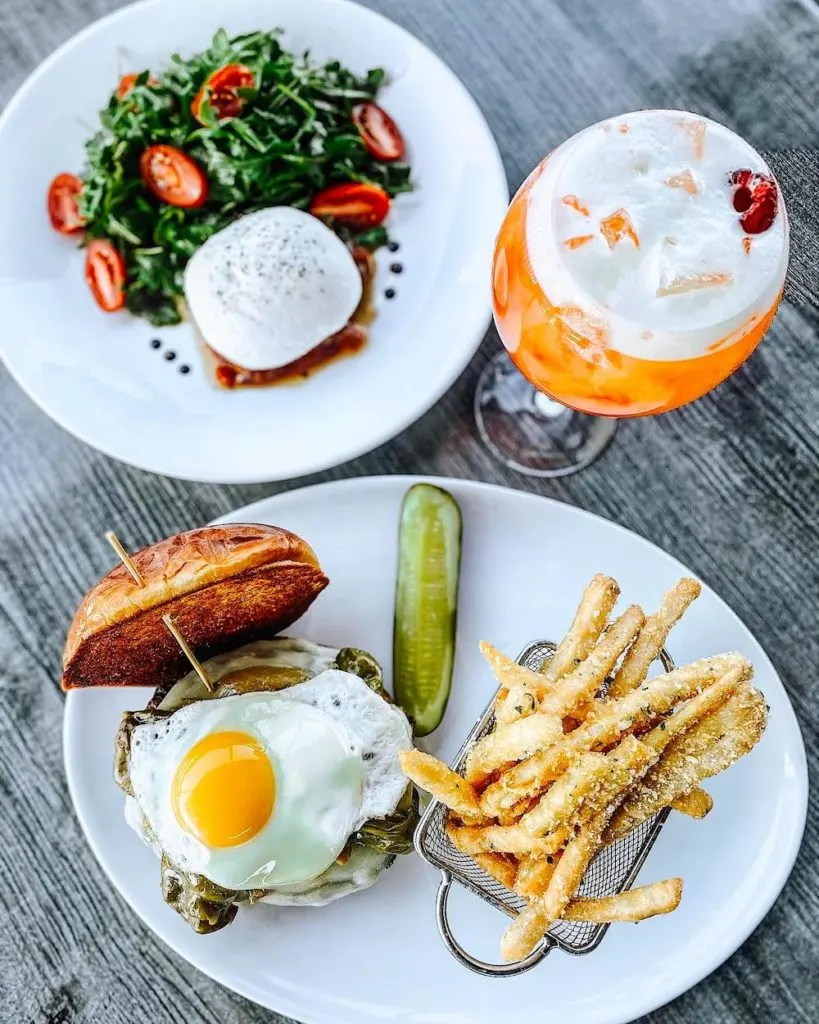 A salad with tomato and, greens and cheese along side a drink  and an open burger with a raspberry from Shadows on the Hudson. Catching a meal here is one of the things to do in Poughkeepsie NY