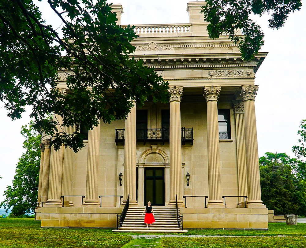 Girl in a red skirt and black shirt standing on the stairs along the exterior of the Vanderbilt Mansion, one of the best things to do in Poughkeepsie NY