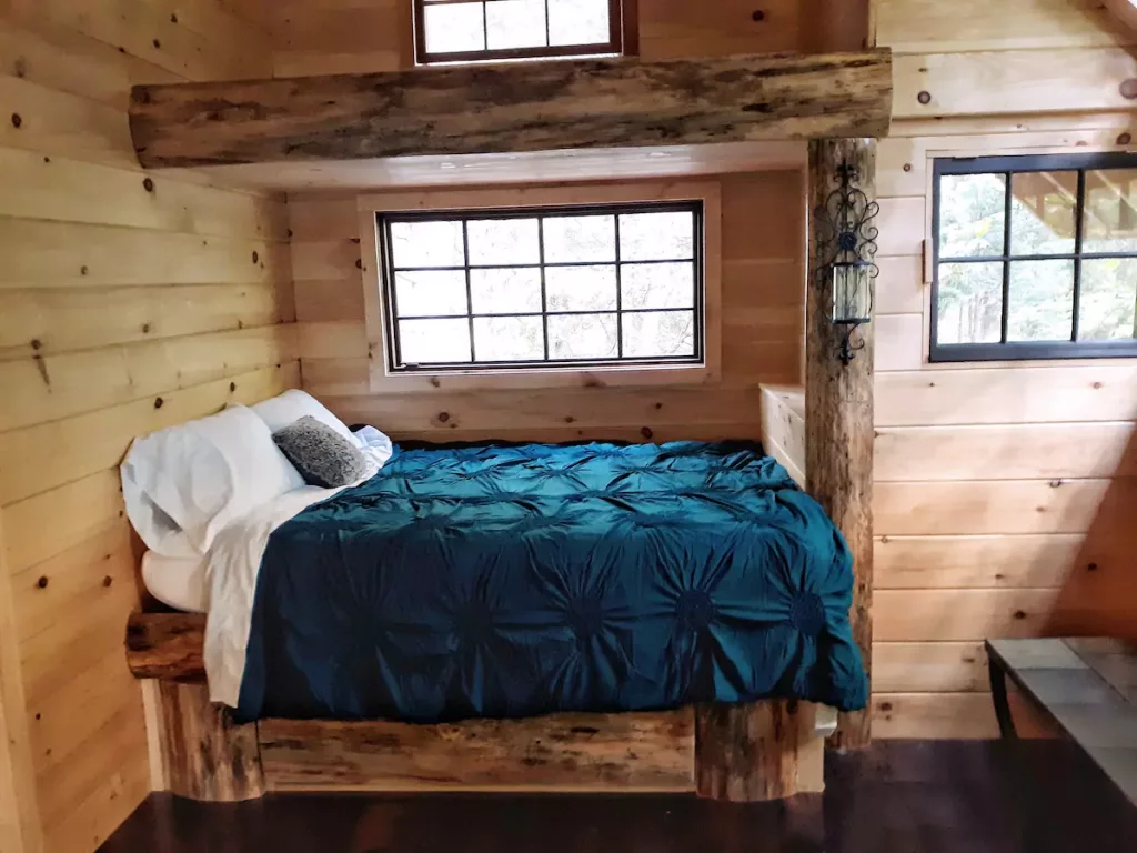 Queen-size bed with a blue duvet inside Adirondack Treehouse rentals NY. 