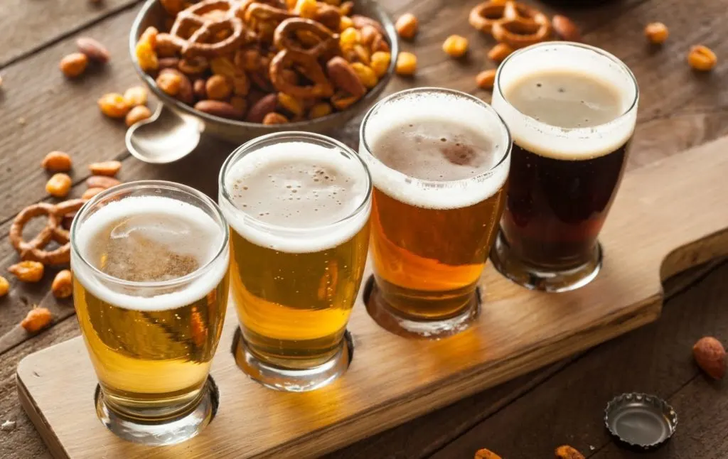 A tasting plate with four beers on it with peanuts and pretzels in the background. 