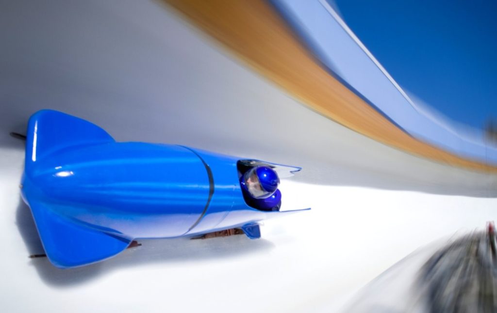 Bright blue bobsled sliding down the track with two passengers in blue helmets, 