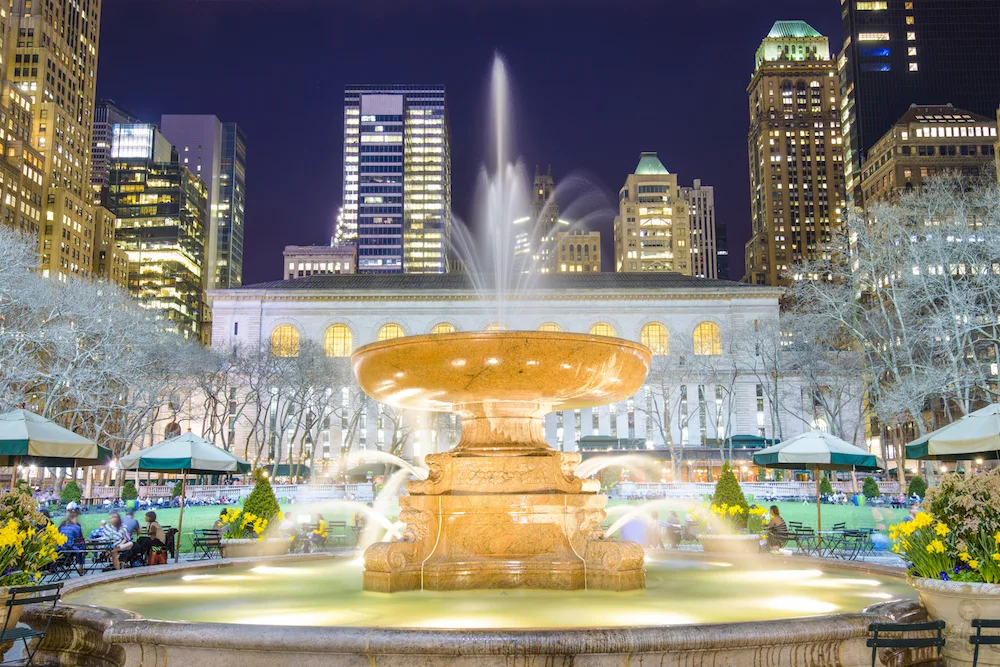 The fountain at Bryant Park in the evening with the New York library in the background.