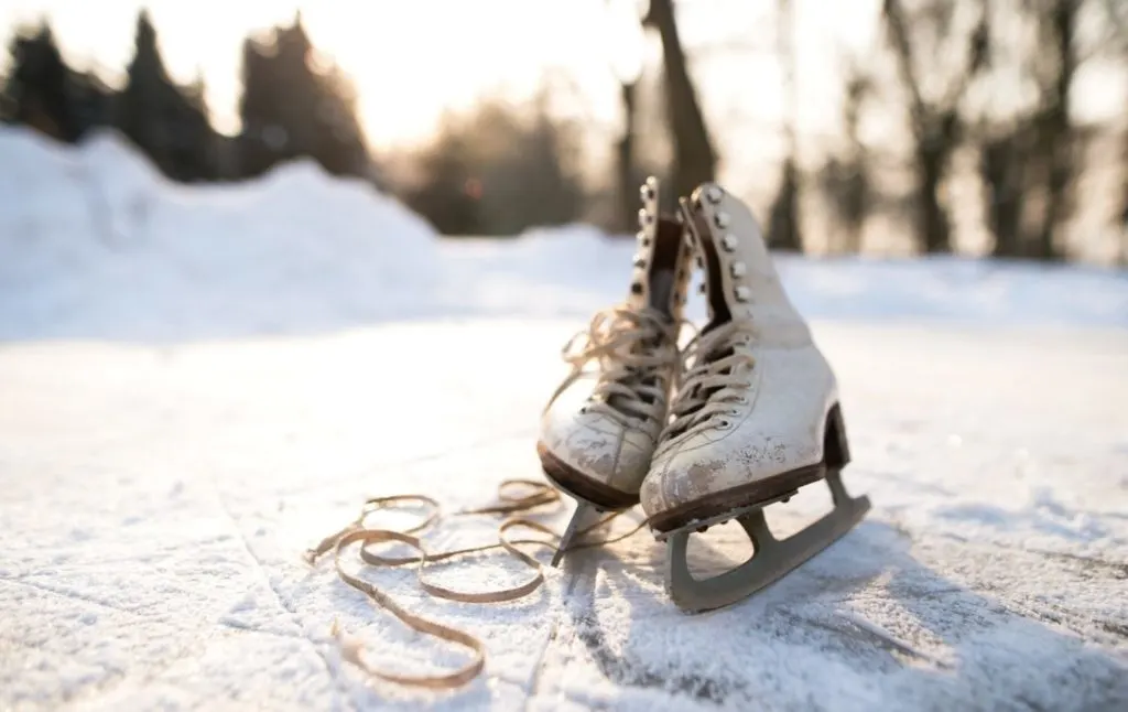 A pair of white figure skates sitting next to one another on a frozen lake with the white laces out front. 