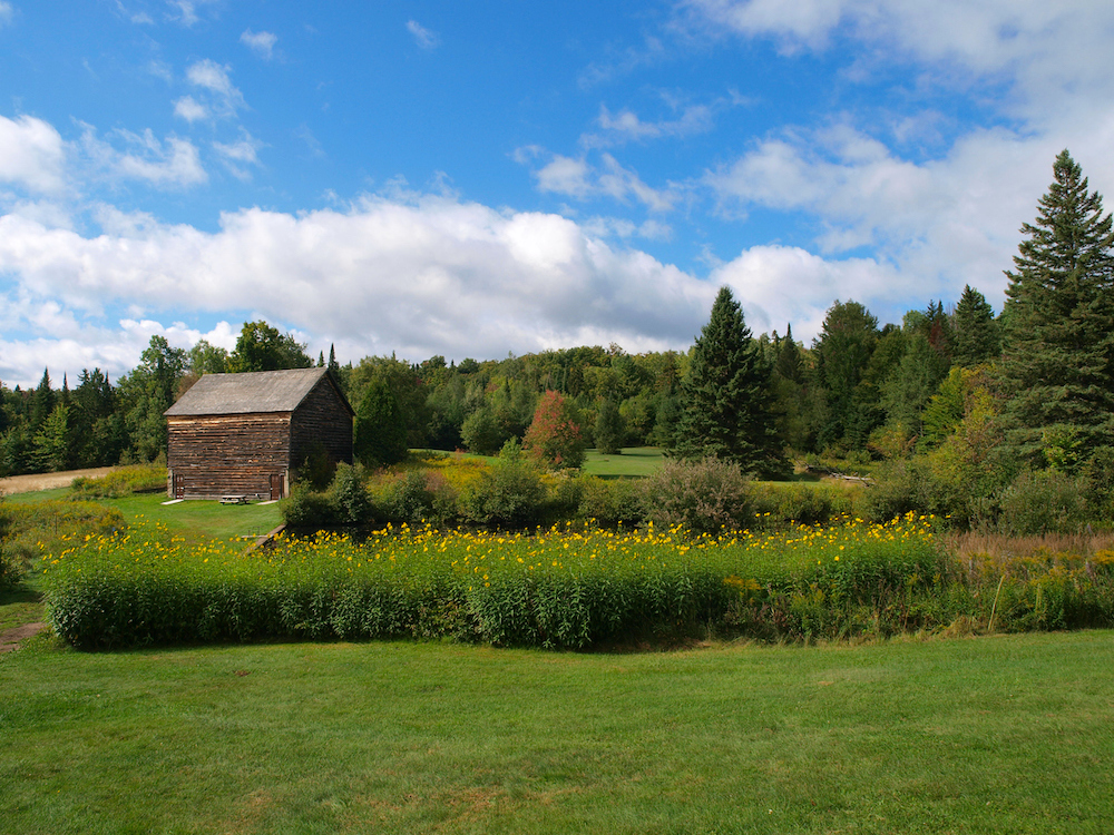 View of the expansive green fields and wooden buildings of the John Brown Farm. This is one of the most unique things to do in Lake Placid, NY. 
