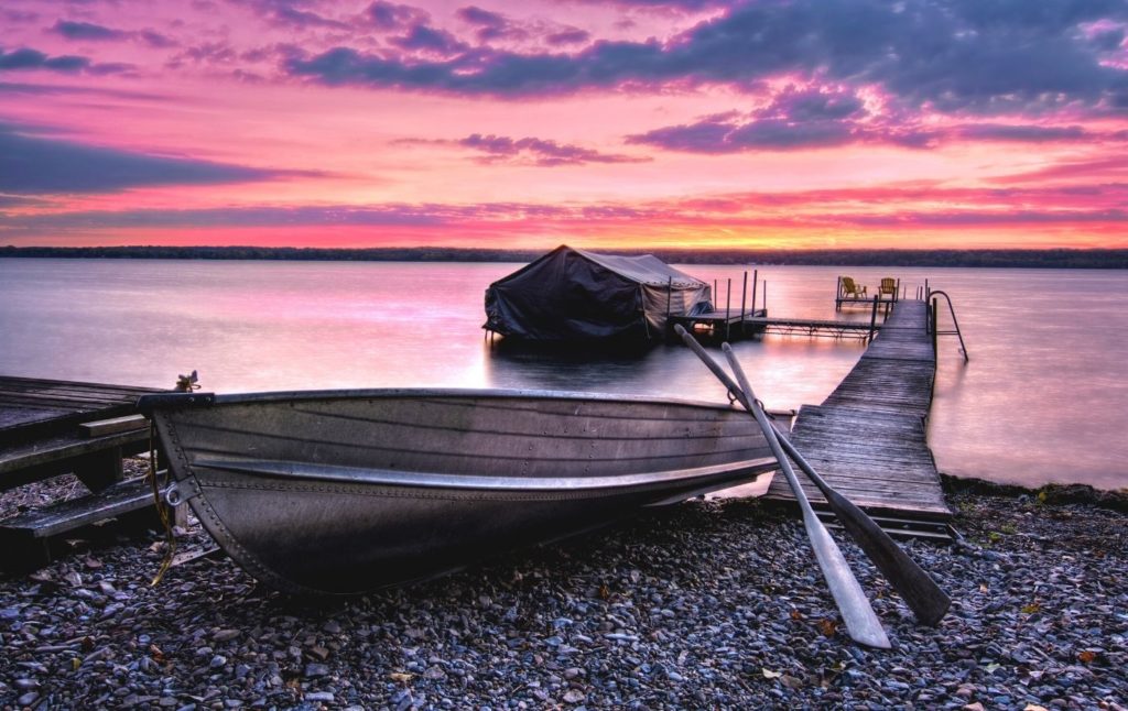 View of Cayuga Lake at sunset with a boat docked on the shores is one of the best lakes in New York.