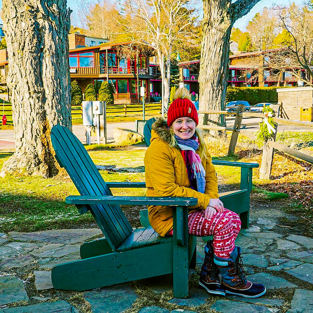 Woman sitting on a green Adirondack chair in winter in Lake Placid.