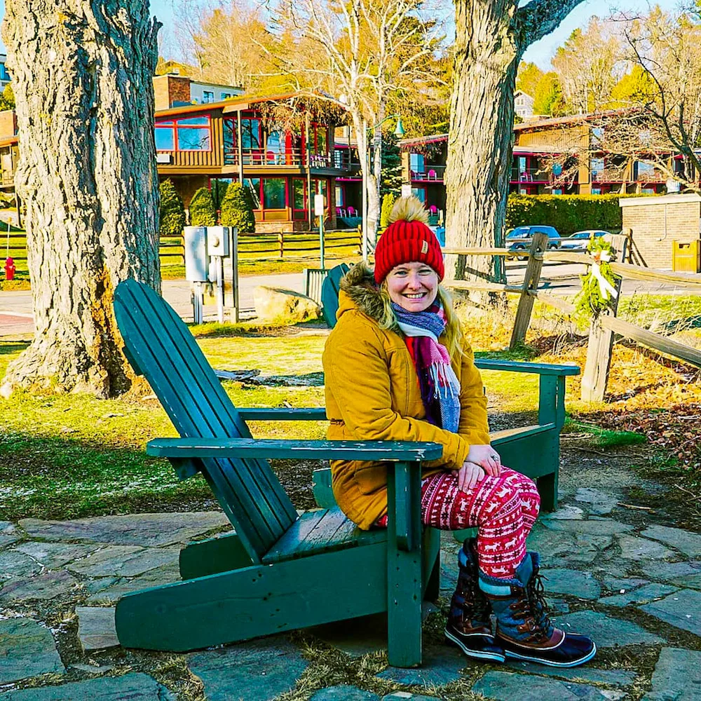 Woman sitting on a green Adirondack chair in winter in Lake Placid. 