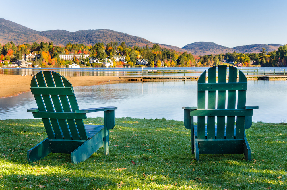 Two green Adirondack chairs in front of Mirror Lake in Lake Placid. 