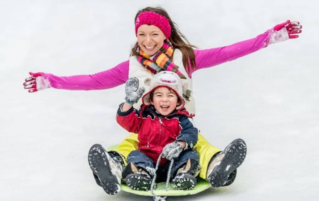 Mother and child sledding together in the winter. 