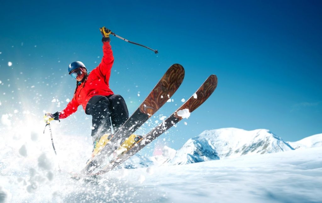 Person in red jacket jumping in the air on skis since skiing is one of the best lake George winter activities.  