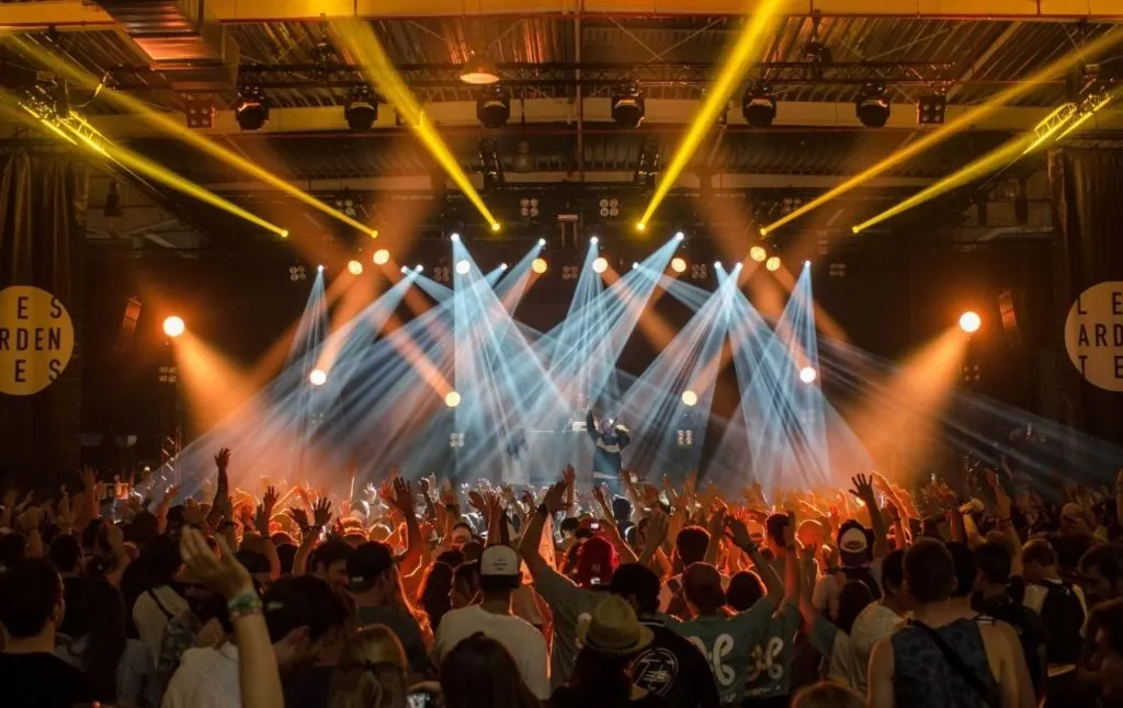 People enjoying a live concert with their hands in the air and a combination of white and yellow light illuminating the room showing just how much music features in the fun things to do in Woodstock NY.