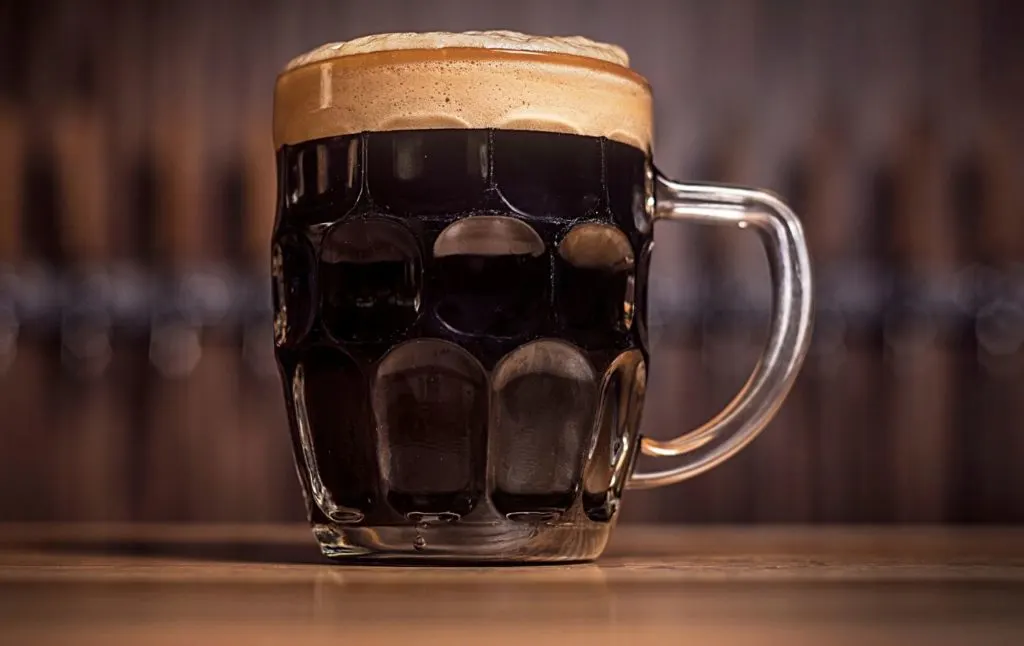 A mug of dark beer sitting on a wooden table. 