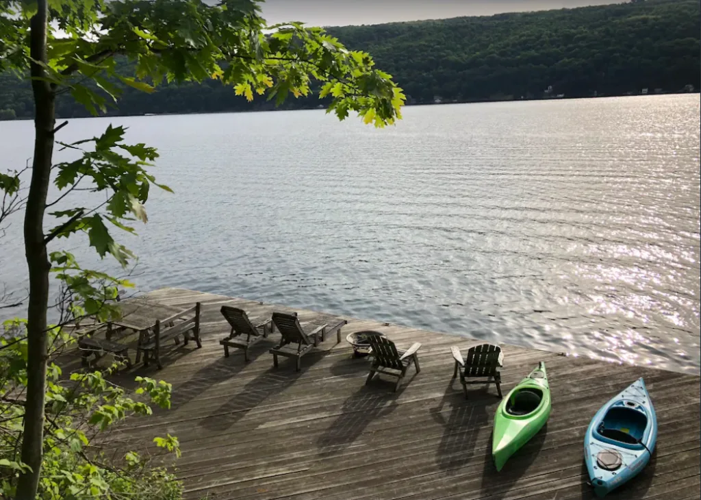 View of Skaneateles Lake from surprisingly spacious historic railcar. Dock with chairs and boats on the lake. 