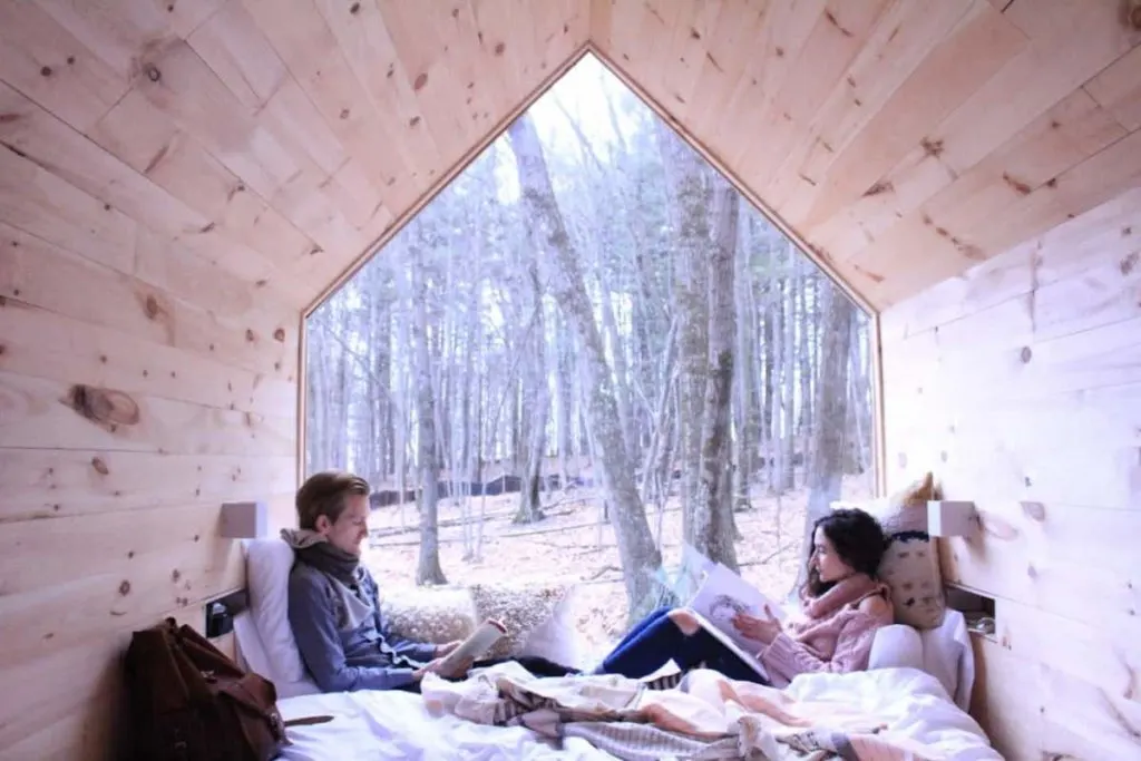 Couple reading while facing one another in bed of the tiny house cabin in Gable Green, New York. 