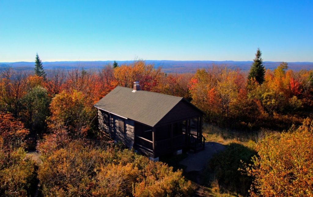 View of fall foliage and a log cabin from the summit of Mount Arab. 