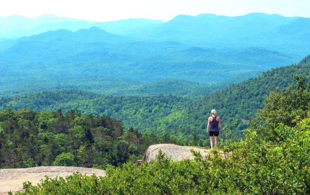 Hiker standing on the summit of Poke-O-Moonshine and enjoying one of the best views in the Adrindacks. 