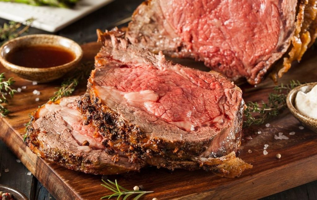 Fresh prime rib on a wooden cutting board with salt and sauce. 