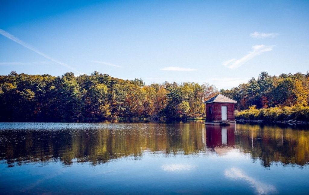 House sitting on Saratoga Lake and the trees on the banks of the lake with a clear sky reflected in the water. 