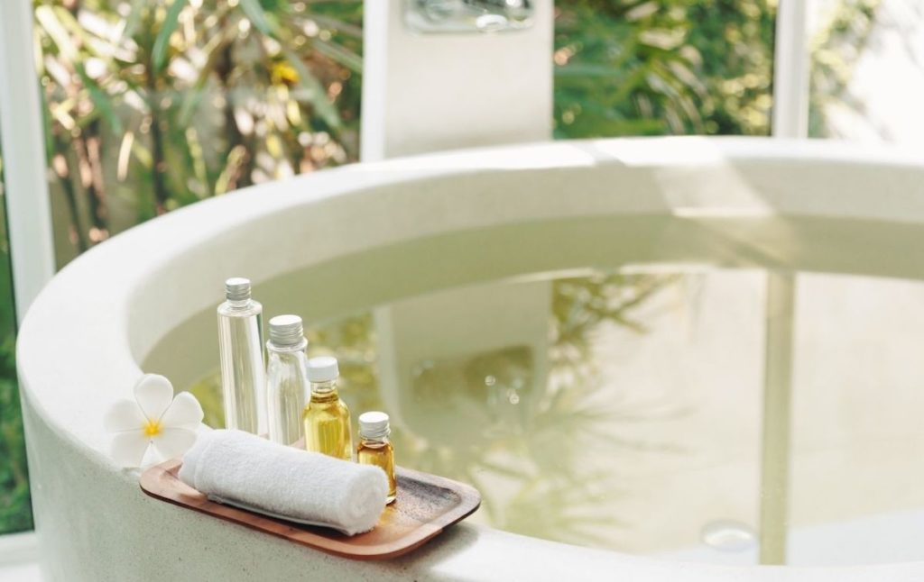 Modern white tub with bath products and a rolled-up white towel. 