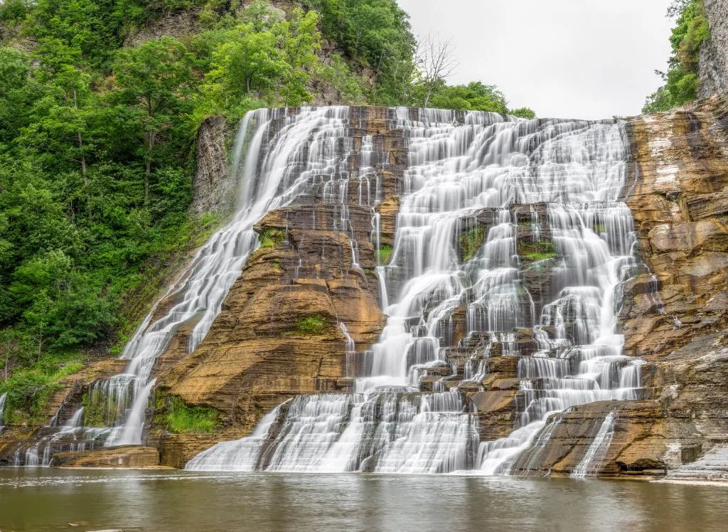 Water flowing off the limestone cliffs with trees surrounding the area. One of the best things to do in Ithaca NY is see Ithaca Falls. 