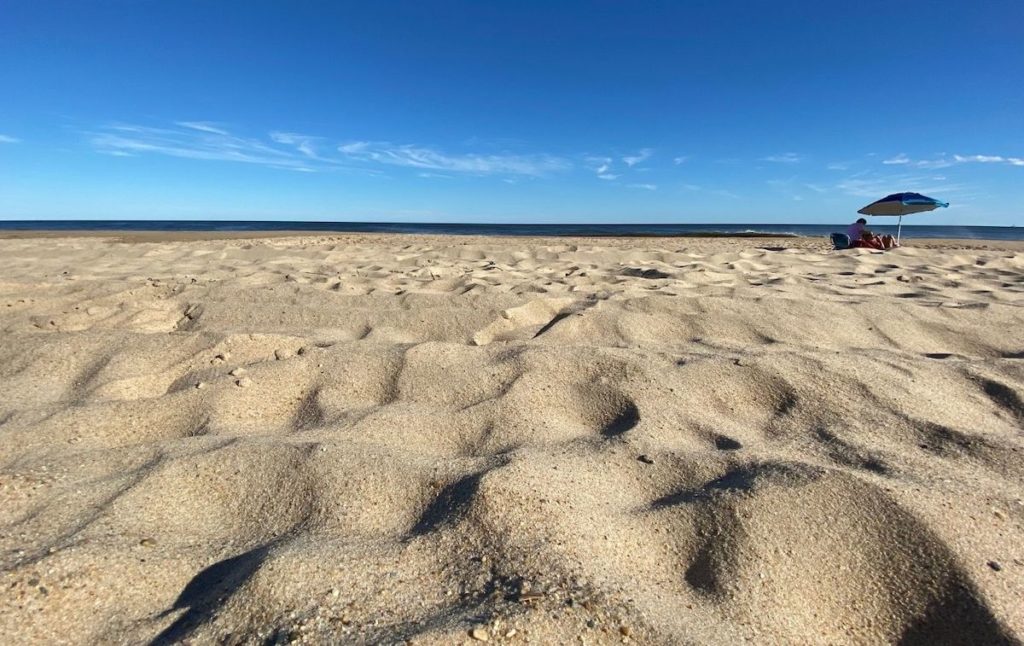 A person sitting on a Montauk beach under an umbrella.  