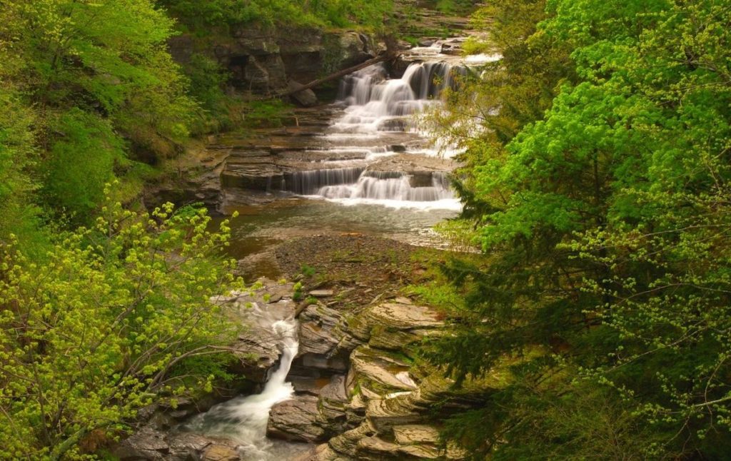 Aerial view of waterfalls in the Catskills region of New York and its rocky path surrounded by green foliage houses some of the top swimming holes in New York. 