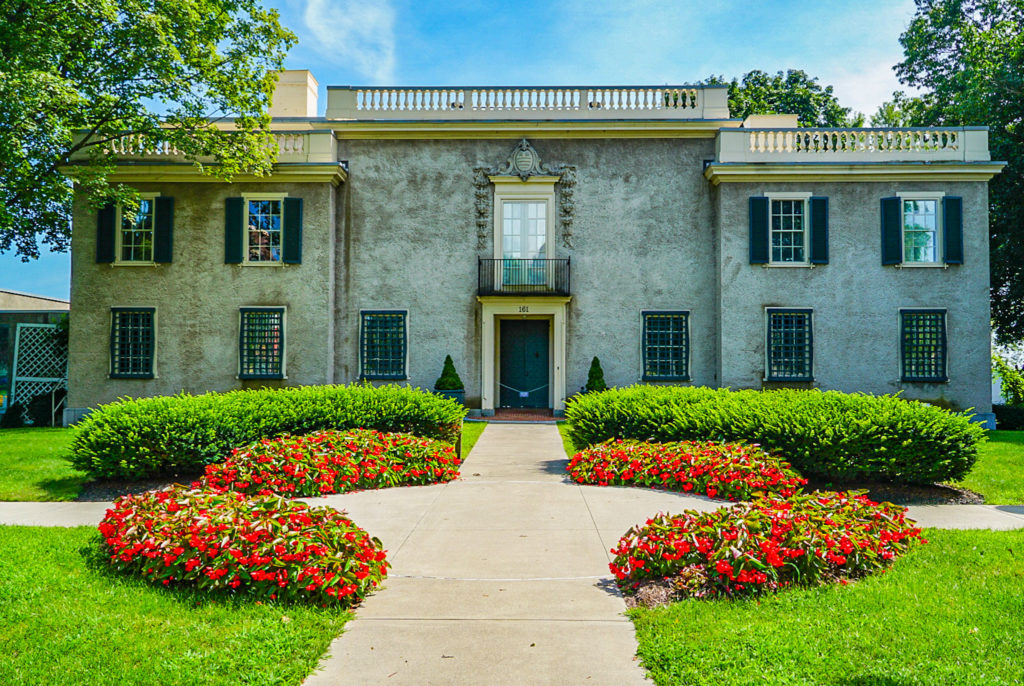 Exterior of the Hyde Collection in Geln Falls with its manicured shrubs, lawns and red flowered bushes.