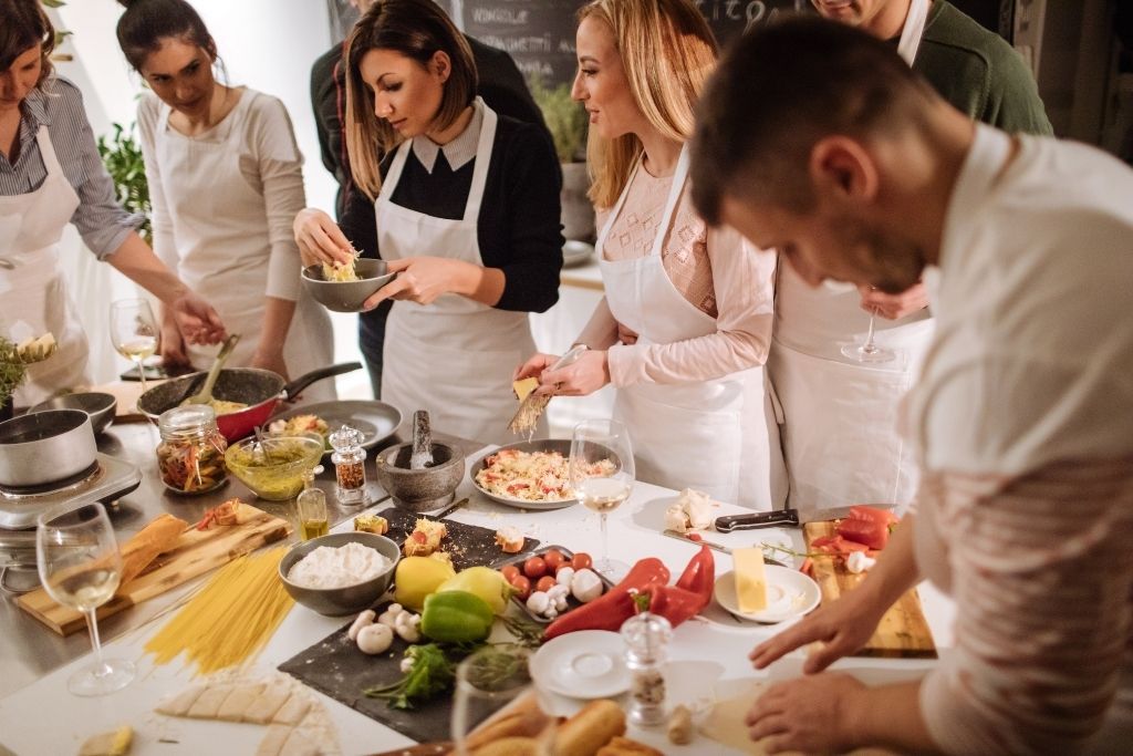 People with white aprons in front of a kitchen platform enjoying a local cooking class as one of the best things to do in NYC for your birthday. 