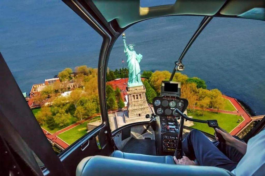 Aerial view of the statue of liberty on liberty island with fall foliage. The view is from the inside of a helicopter cockpit and takes places during the best NYC helicopter tour. 