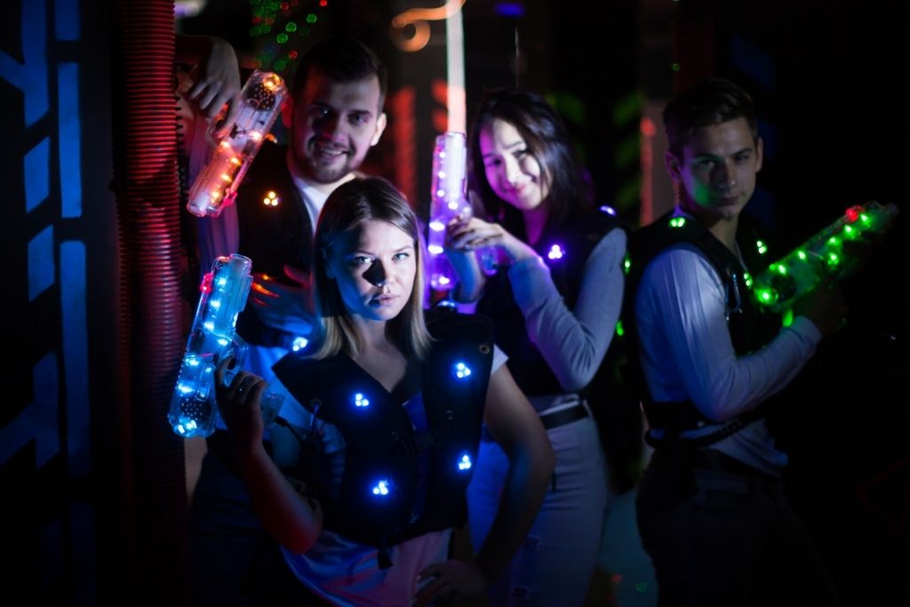 Men and women playing laser tag with the lights on their laser guns and vest lit up, one of the best birthday ideas NYC has to offer. 