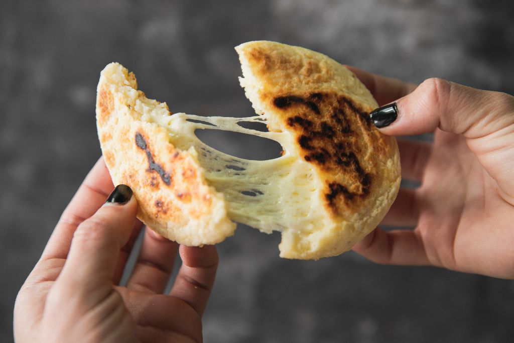 Person holding an arepa with melty cheese in the middle from one of the best Brooklyn coffee shops. 