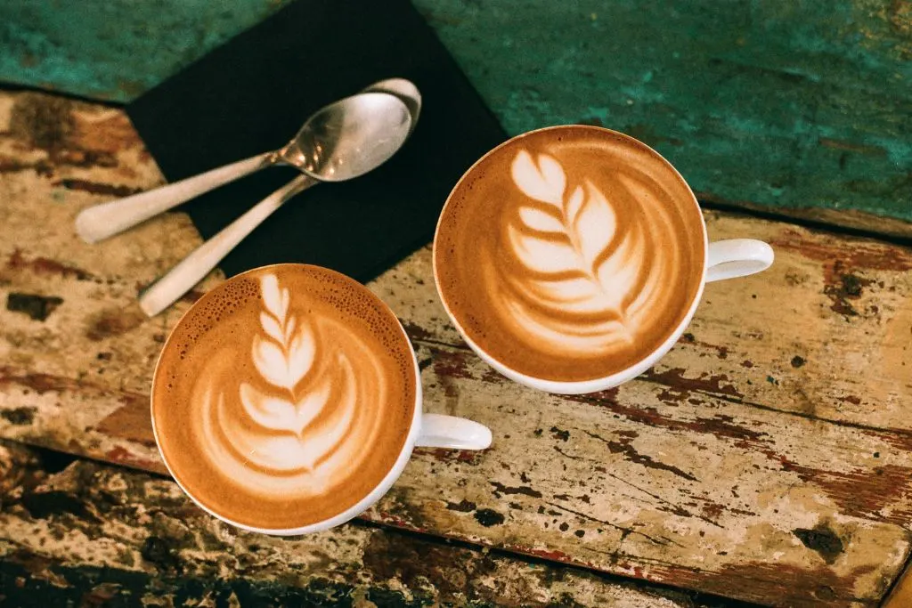 Two lattes on a wooden tables with spoons from one of the many cute cafes in NYC.