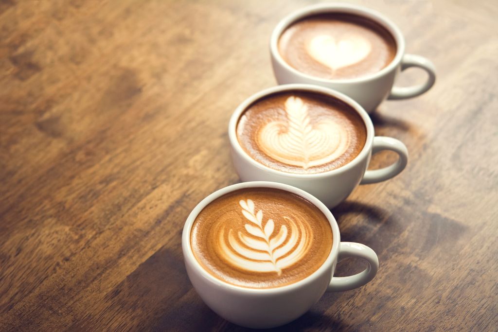 Three lattes lined up on a wooden table. 