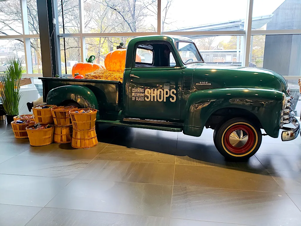 View of a vintage green pick up truckwith glass pumpkins in the back in Corning. One of the best places to visit in uptstate NY.