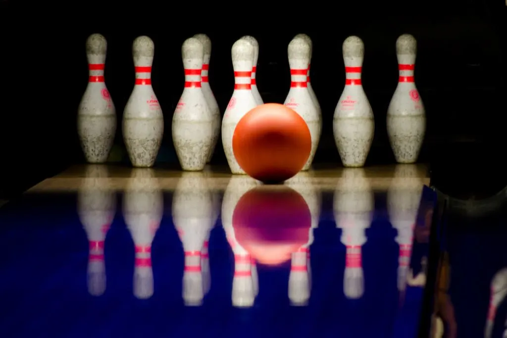 Orange bowling ball hitting some bowling pins in nyc after midnight. 