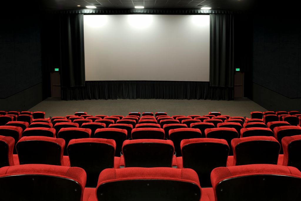 Move theater with a giant white screen and red seats. 