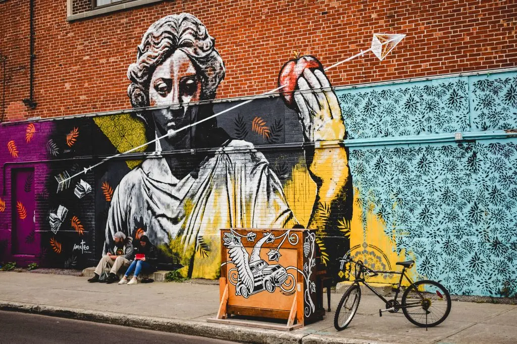 Two people sitting in front of a street art mural with an angel after enjoying many Kingston NY things to do. 