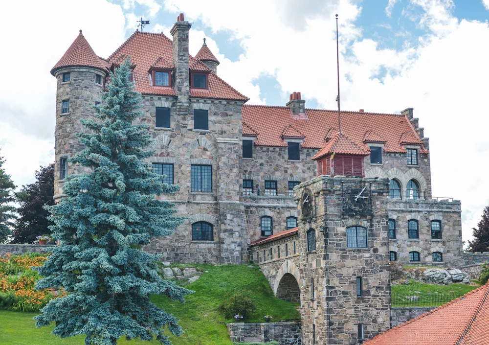 View of the stone exterior and red roof of Singer Castle, which is an essential part of your Alexandria Bay Ny itinerary. 