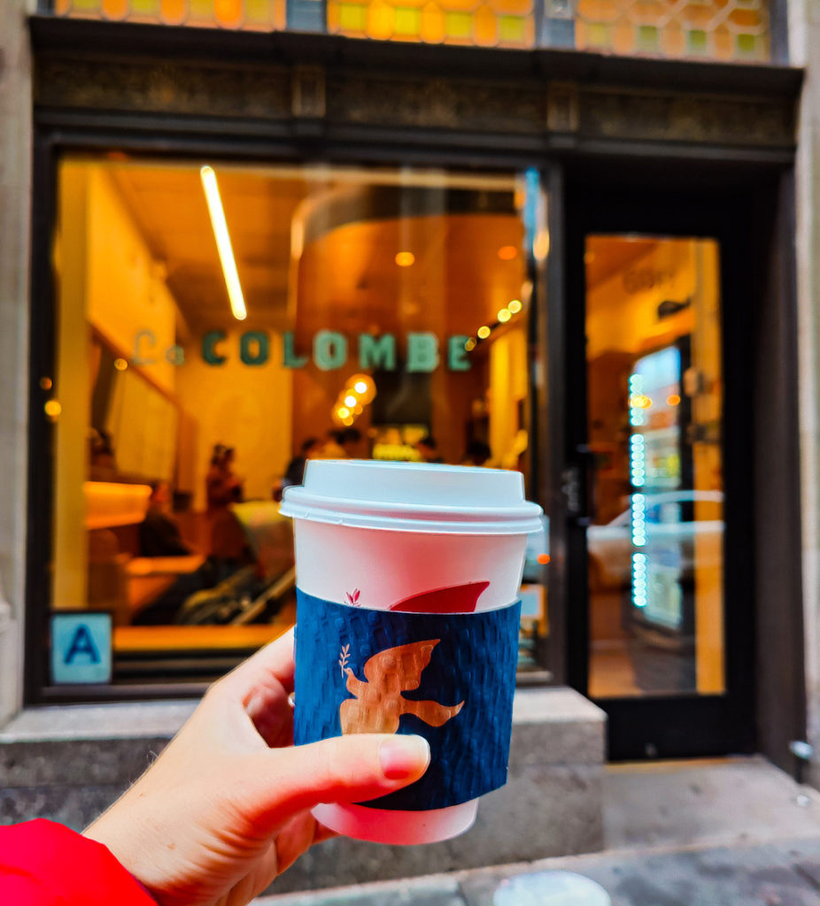 Holding a to-go cup of coffee in front of the La Colombe Coffee Roasters storefront. 