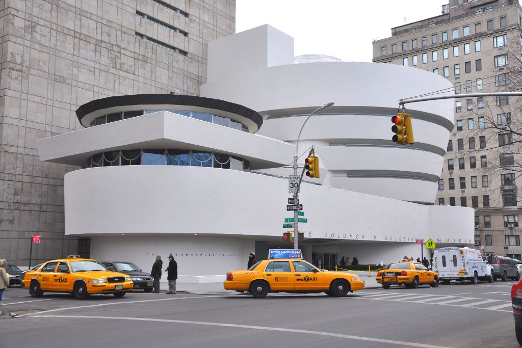 Modern white exterior of the Guggenheim on Fifth Avenue with yellow cabs out front. 