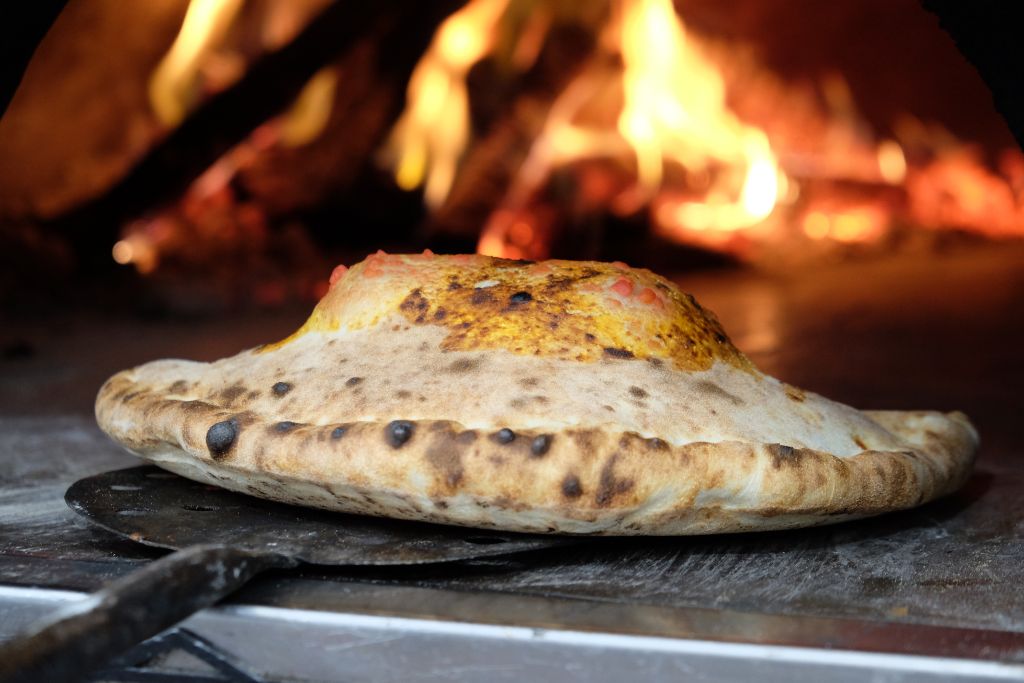 Authenic calzone being baked in the fire in a wood burning oven. 