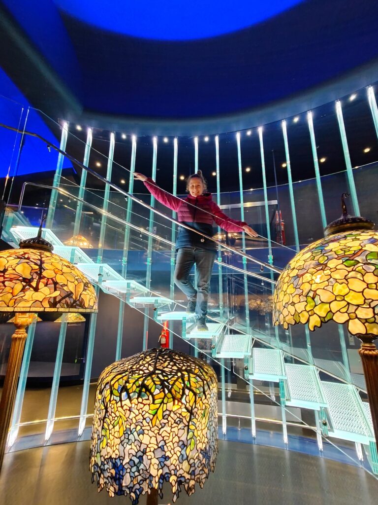 Me standing on the iconic staircase surrounded by Tiffany lamps inside the New York Historical.