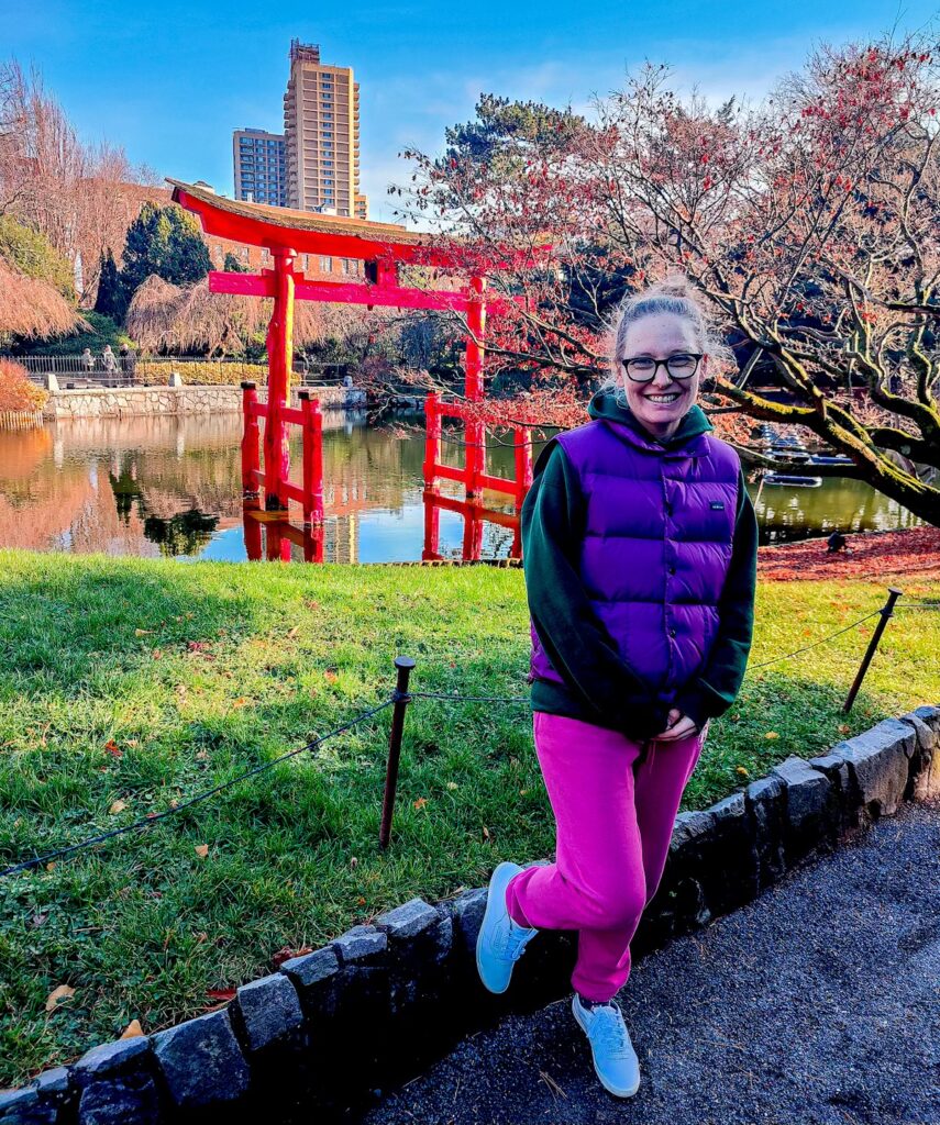View of me standing in a purple vest and pink sweat pants in front of a red gate at Brooklyn Botanic Garden. This should help you decide what to wear in NYC in the spring. 
