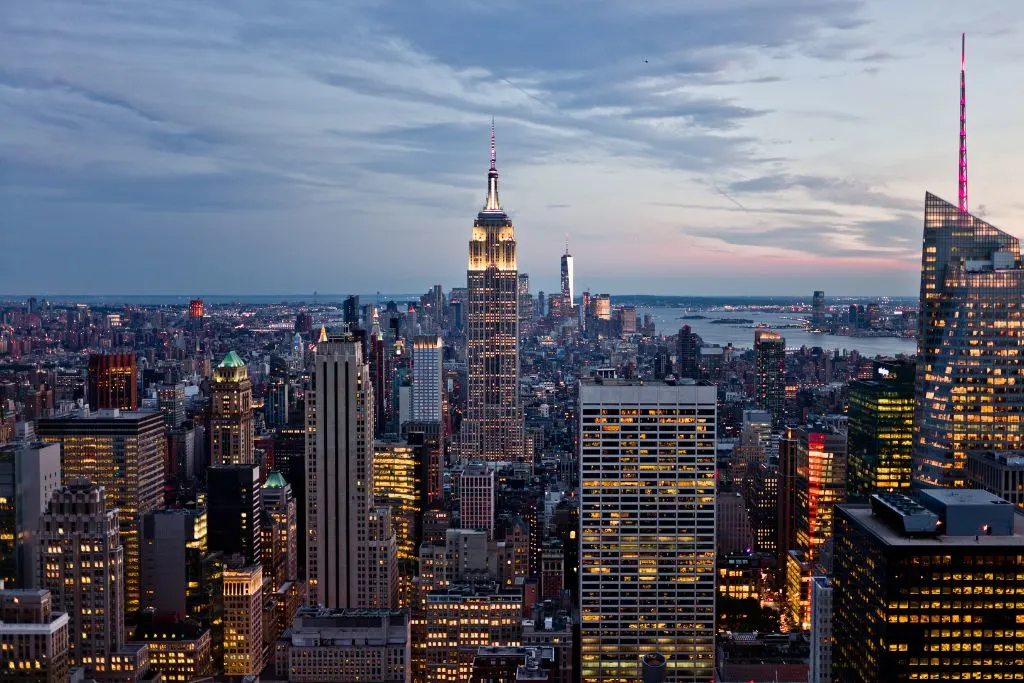 View of the Empire State Building with white lights coming on in the evening and the sky getting dark in New York City,. This is an aerial show of the Empire State Building straight on.