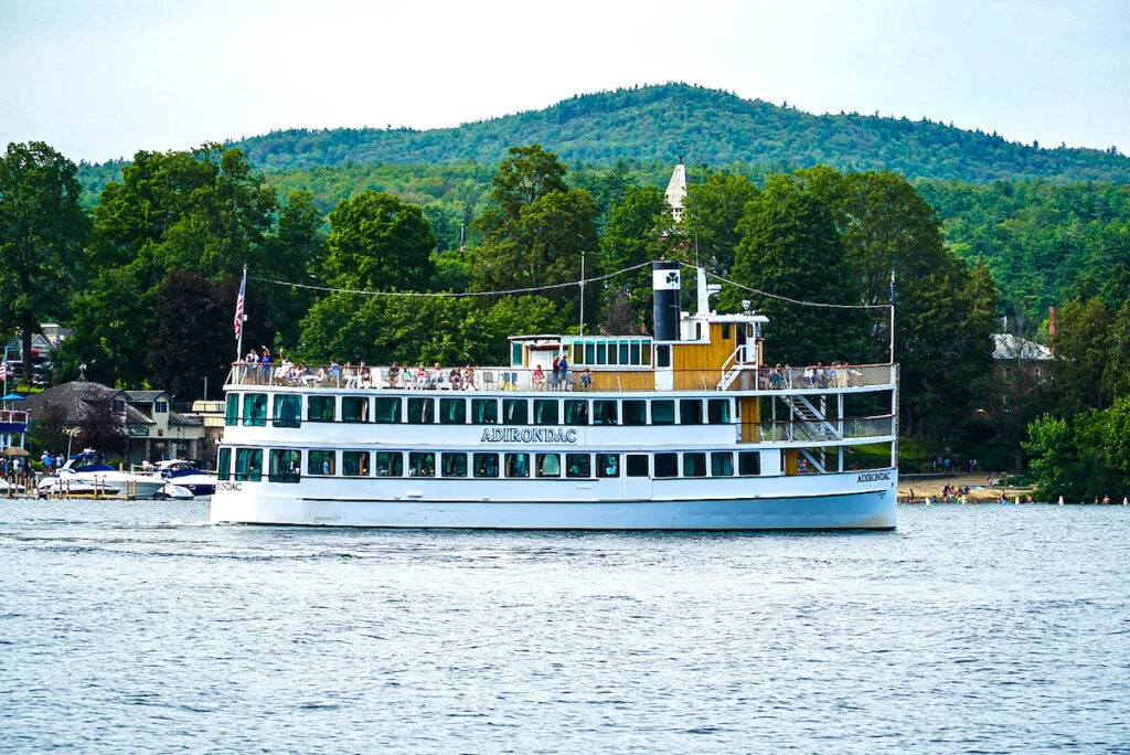 View of a vinatge white steamboat cruising through Lake George with the Adirondack Mountains in the background. This is one of the best things to do in Lake George NY. 
