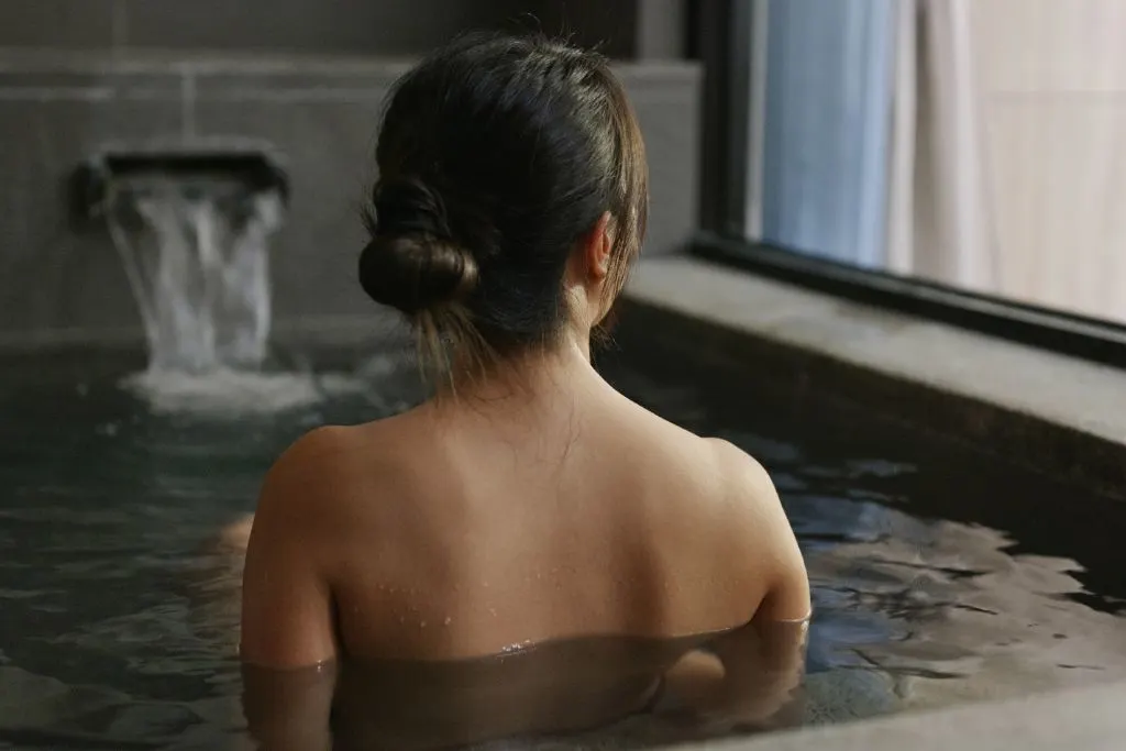 Women with black hair looking away from the camera with her back to use ad sitting in a thermal pool in a Korean spa.