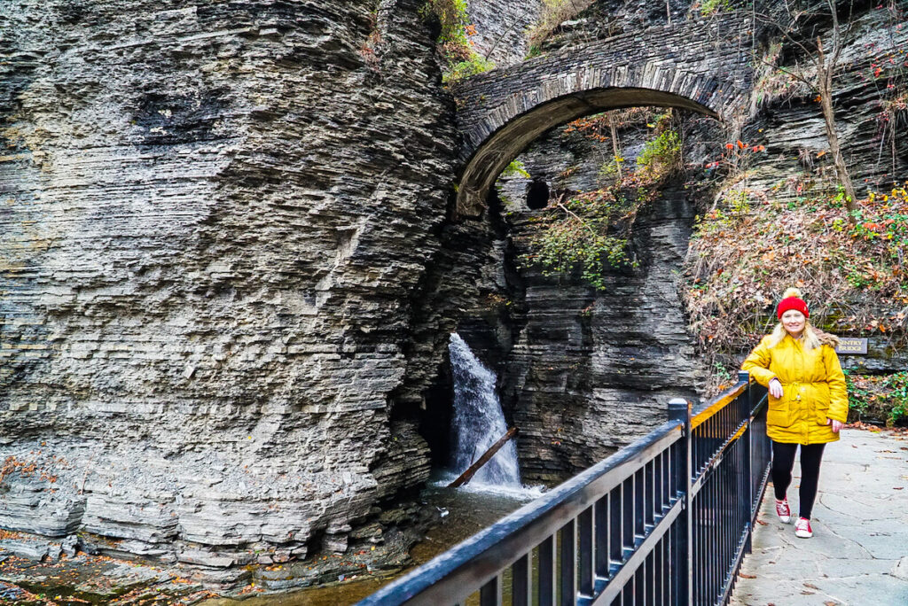 Me standing on the Gorge Trail at Watkins Glen. I am wearing a yellow jacket and a red hat in front of one of the best places to visit in upstate NY.
