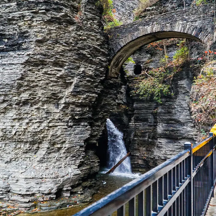 Me standing on the Gorge Trail at Watkins Glen. I am wearing a yellow jacket and a red hat in front of one of the best places to visit in upstate NY.